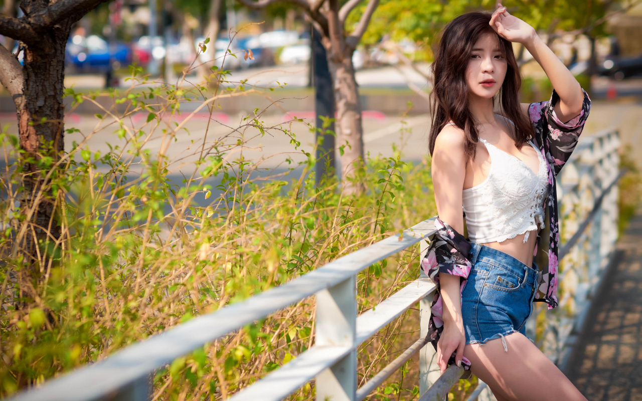 Молодая азиатка в синих шортах стоит у забора