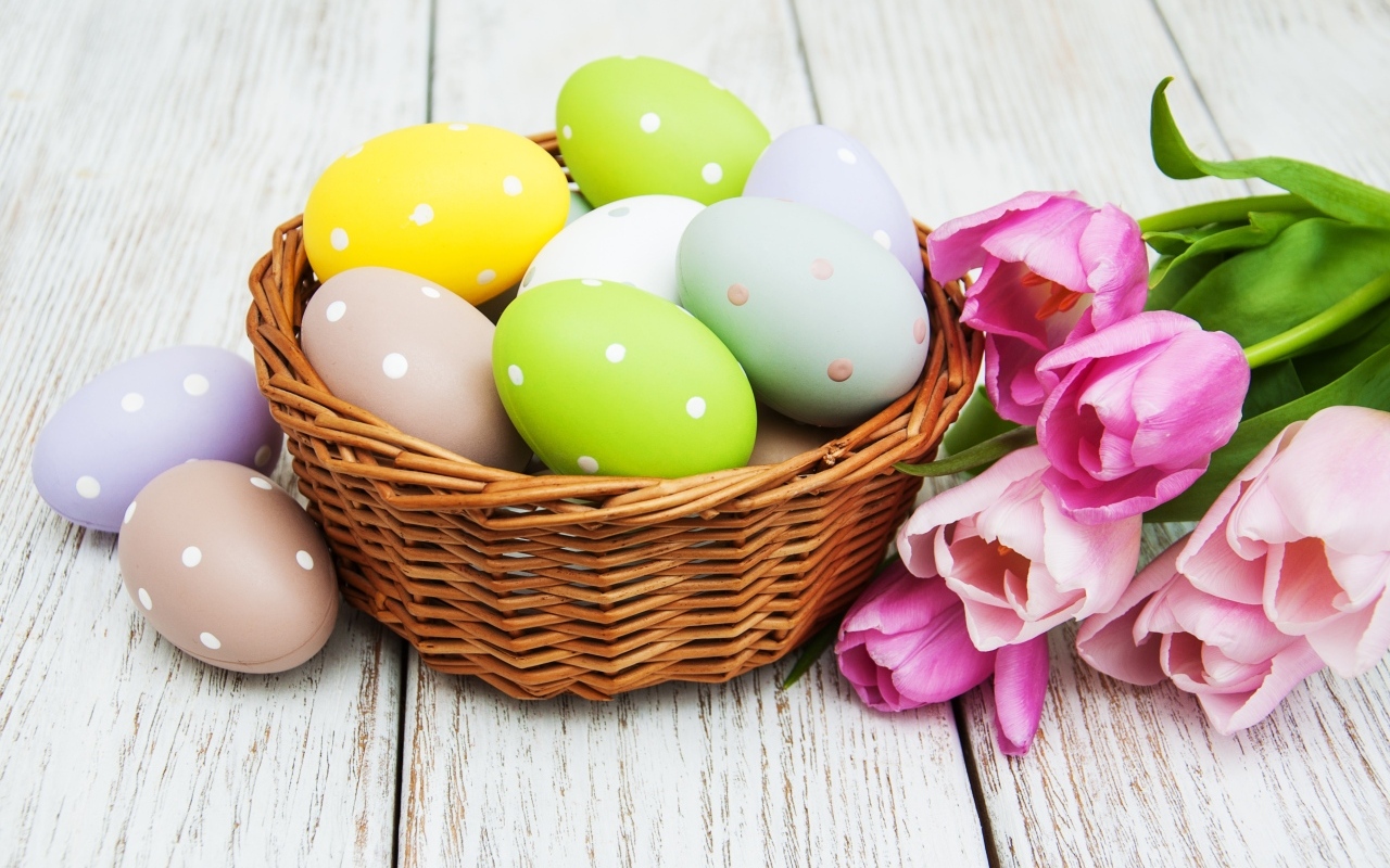 Корзина разноцветных яиц с тюльпанами на столе на Пасху