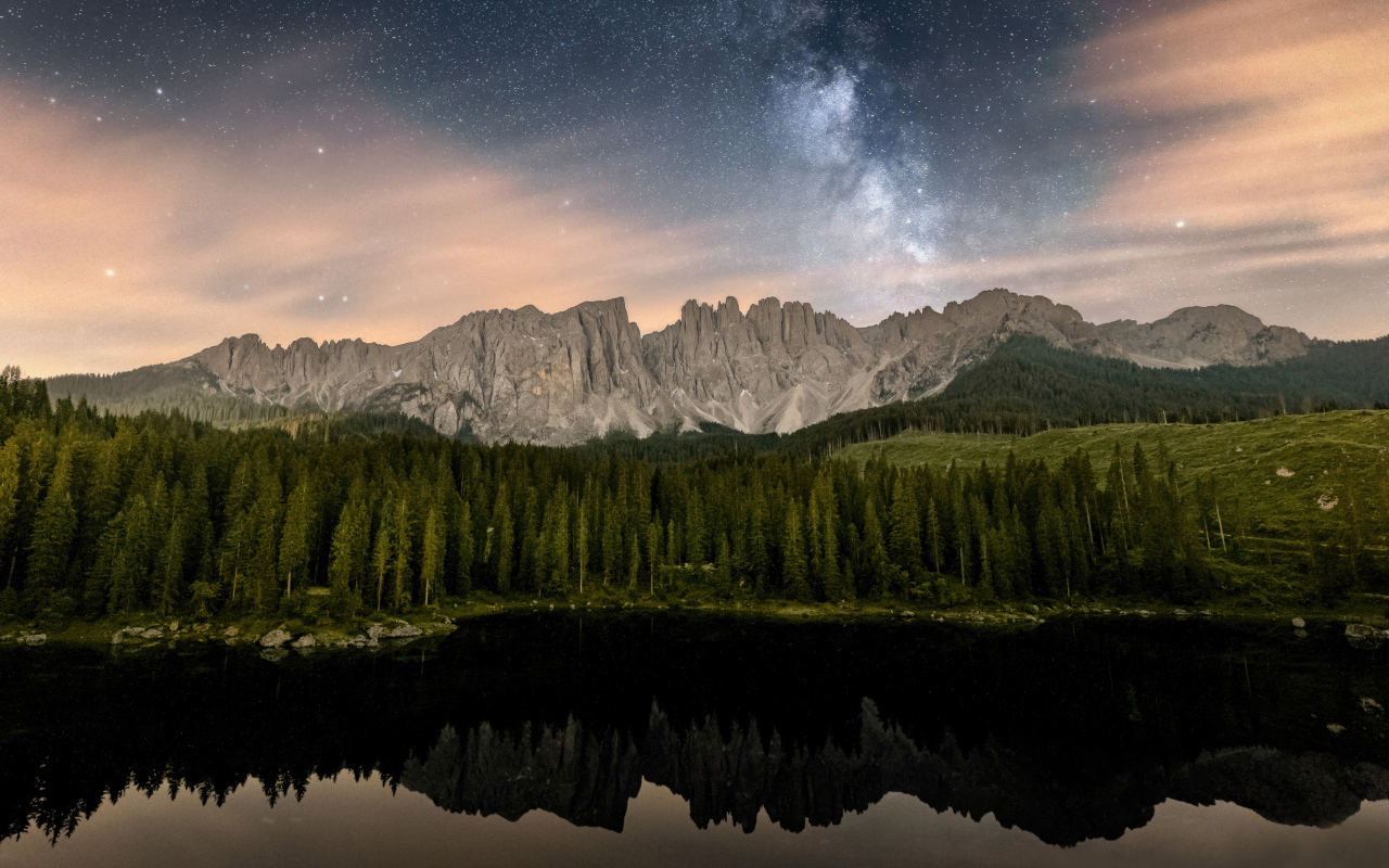 Млечный путь над горами и лесом отражающимися в воде
