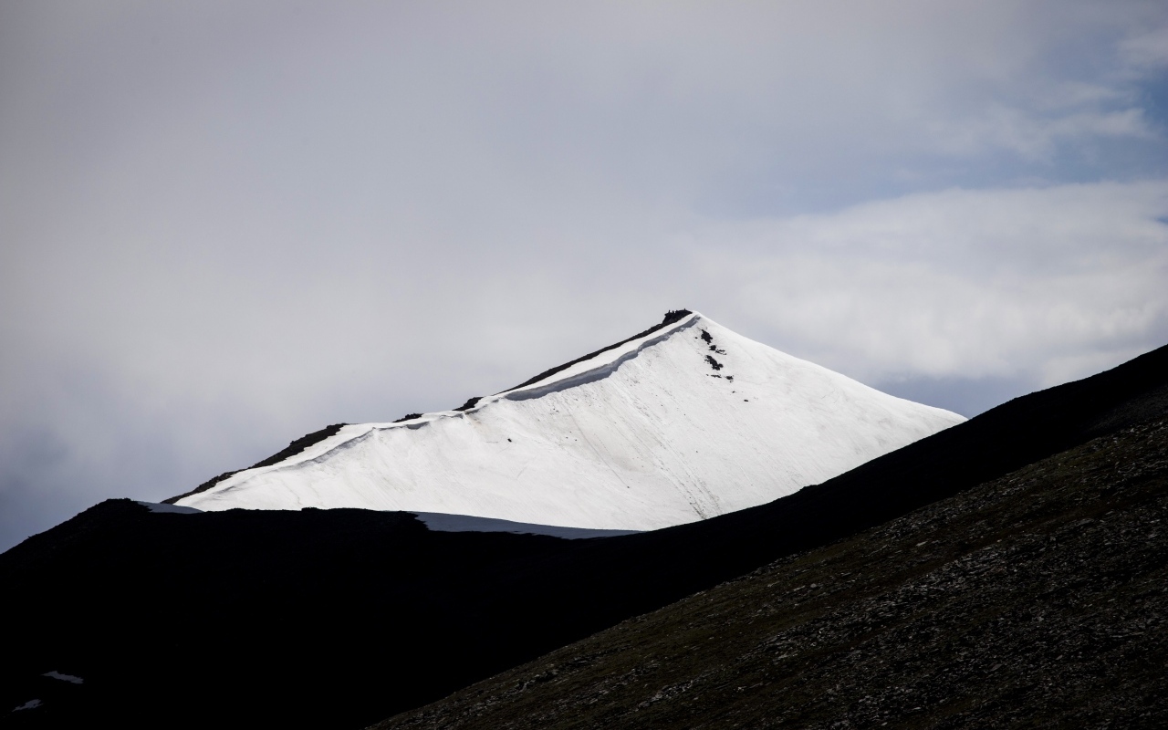Заснеженная вершина горы под грозовым небом
