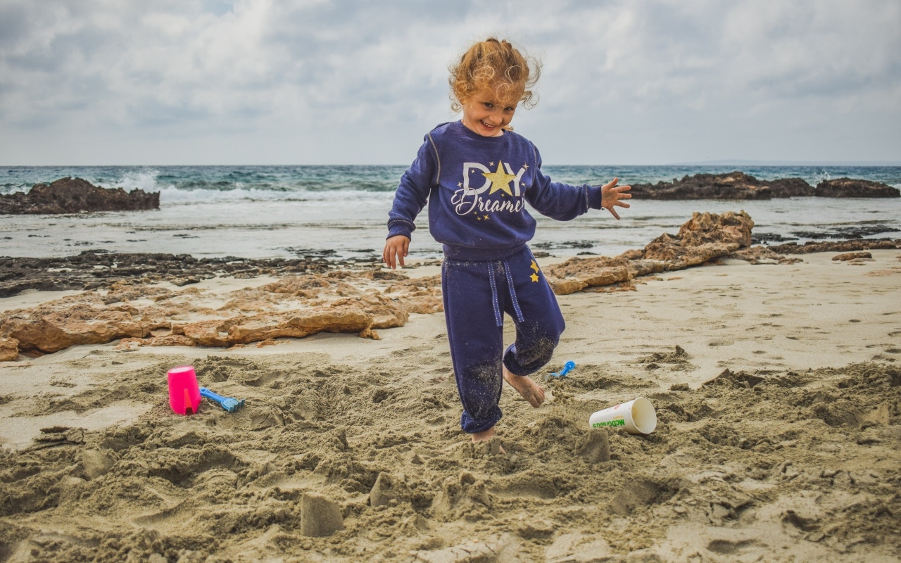 Веселая девочка играет на песке на пляже