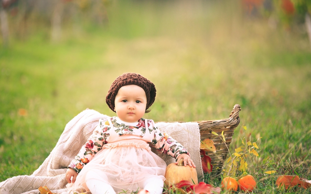 Милая маленькая девочка в шапке сидит на траве 