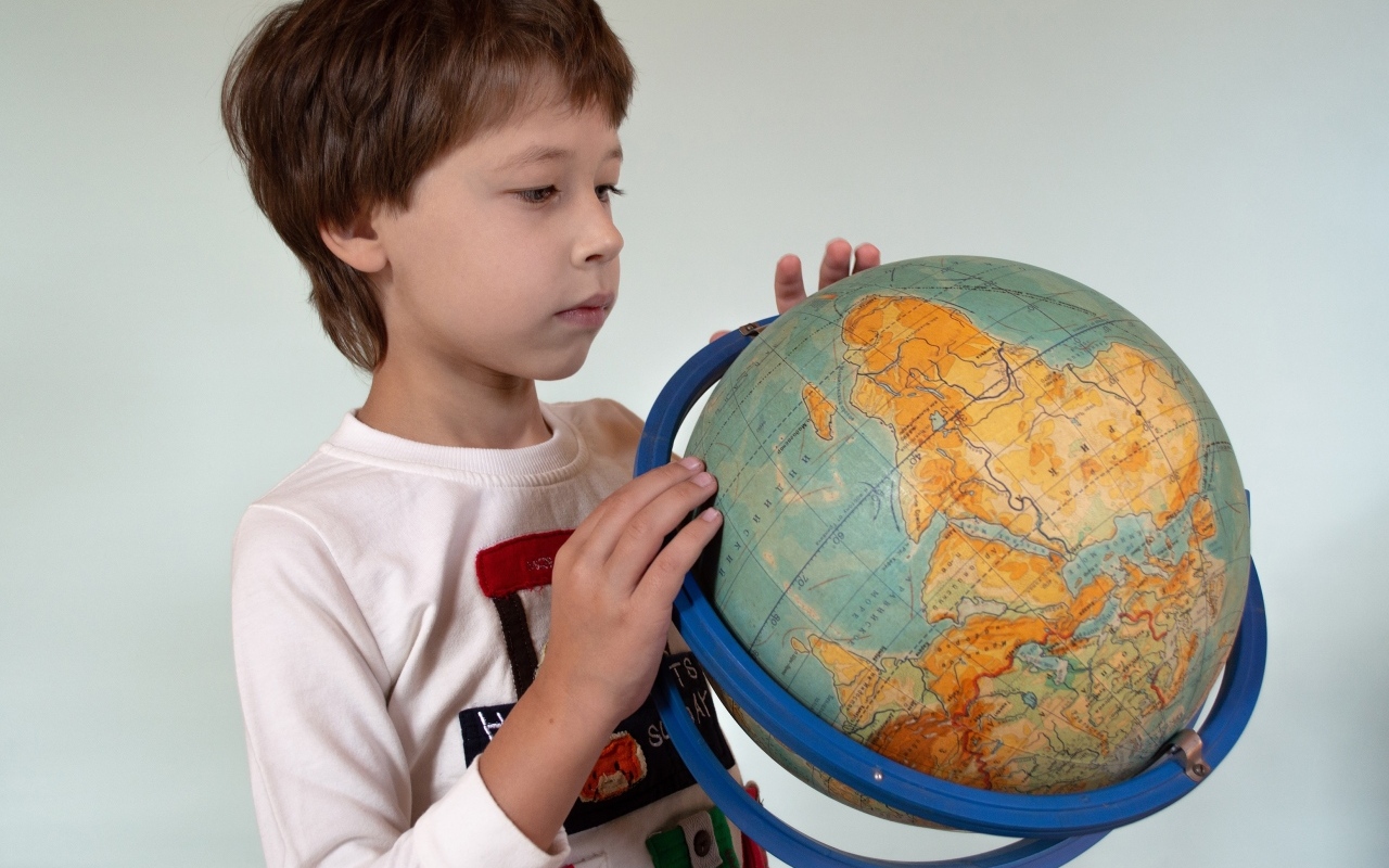 Школьник изучает глобус на сером фоне