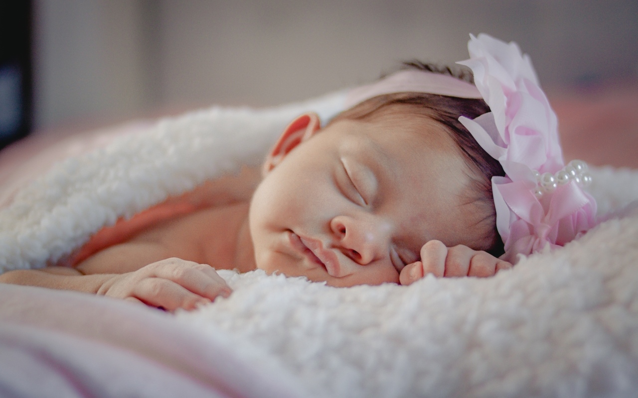 Спящая новорожденная девочка с розовым бантом на голове