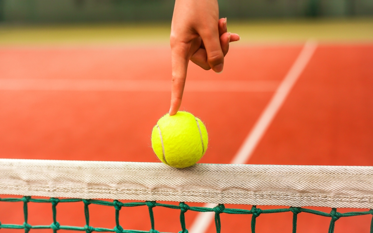 Палец держит желтый теннисный мяч