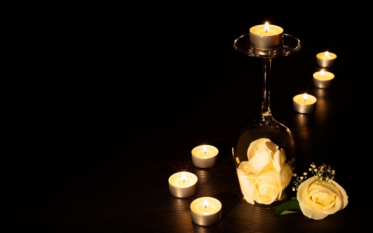 Зажженные свечи с цветами розы на черном фоне