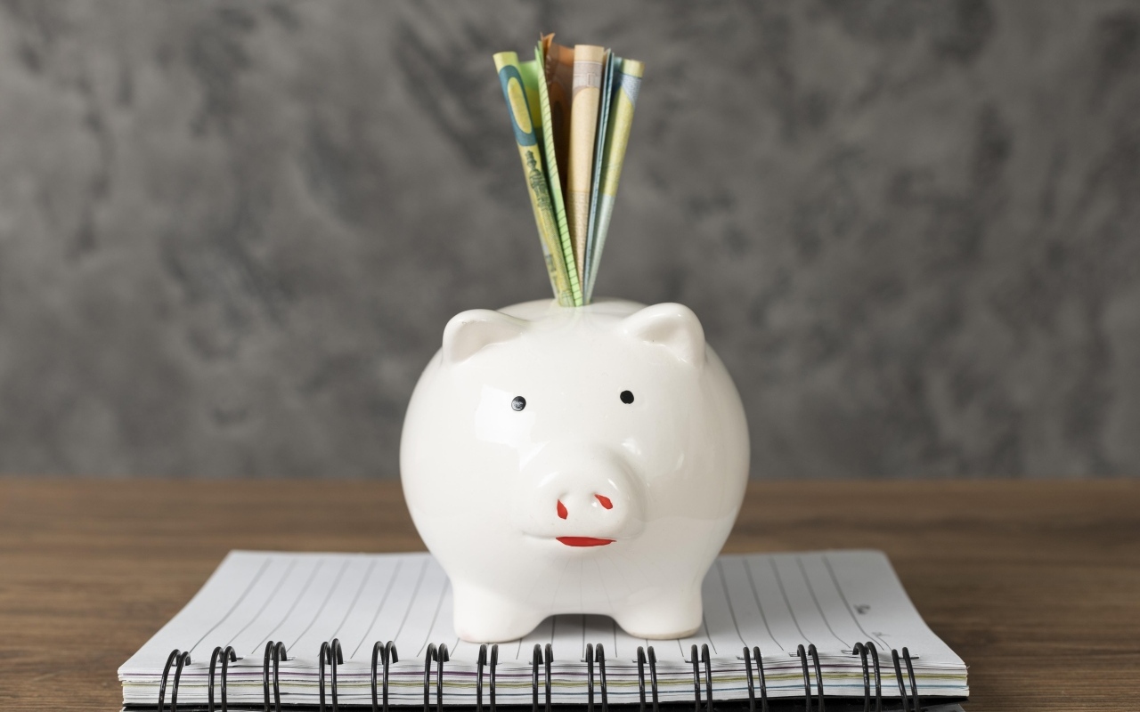 Свинья копилка с купюрами на столе с блокнотом