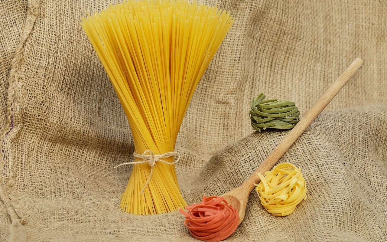 Разноцветные макаронные изделия с деревянной ложкой на мешке