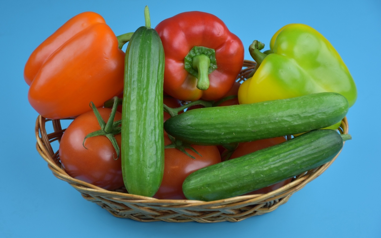 Перец, помидоры и огурцы в корзине на голубом фоне
