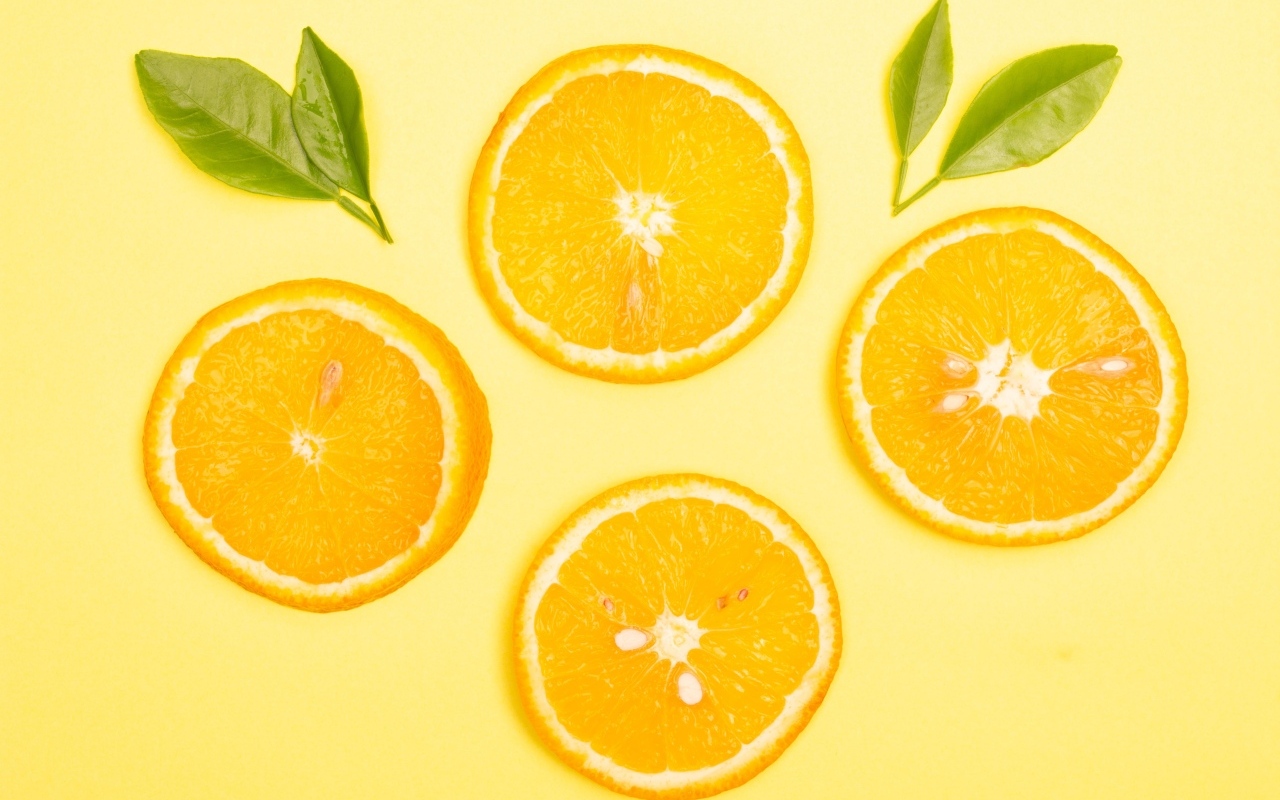 Нарезанный апельсин с зелеными листьями на желтом фоне