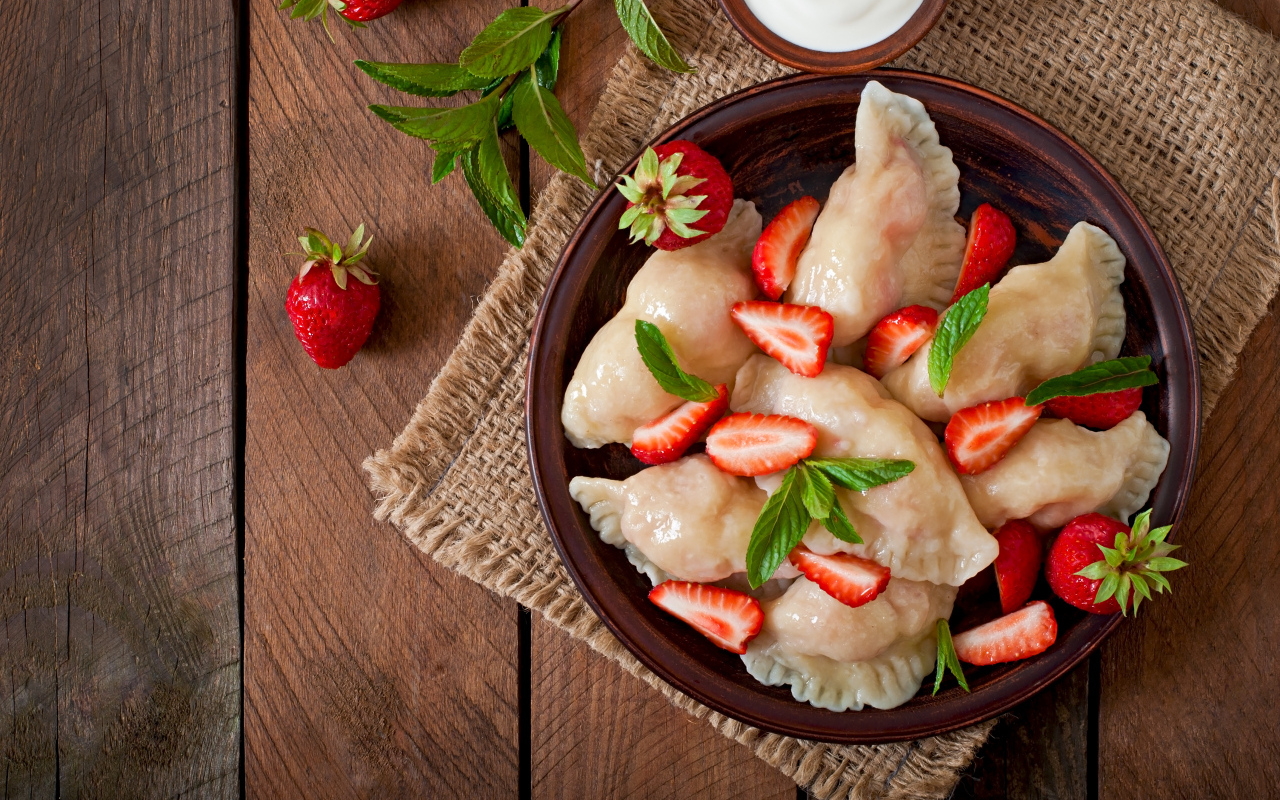 Вареники с клубникой на столе со сметаной