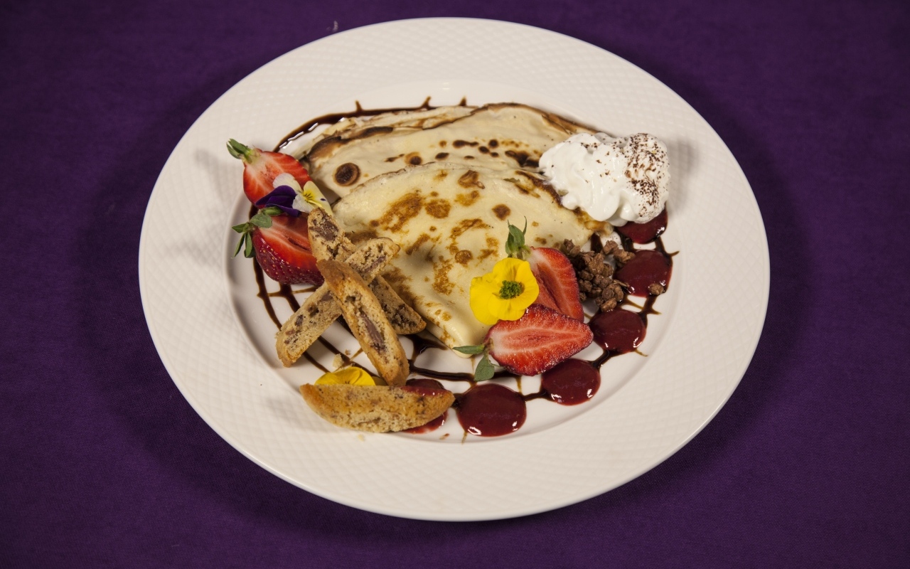 Тонкие блинчики с кремом и ягодами на тарелке