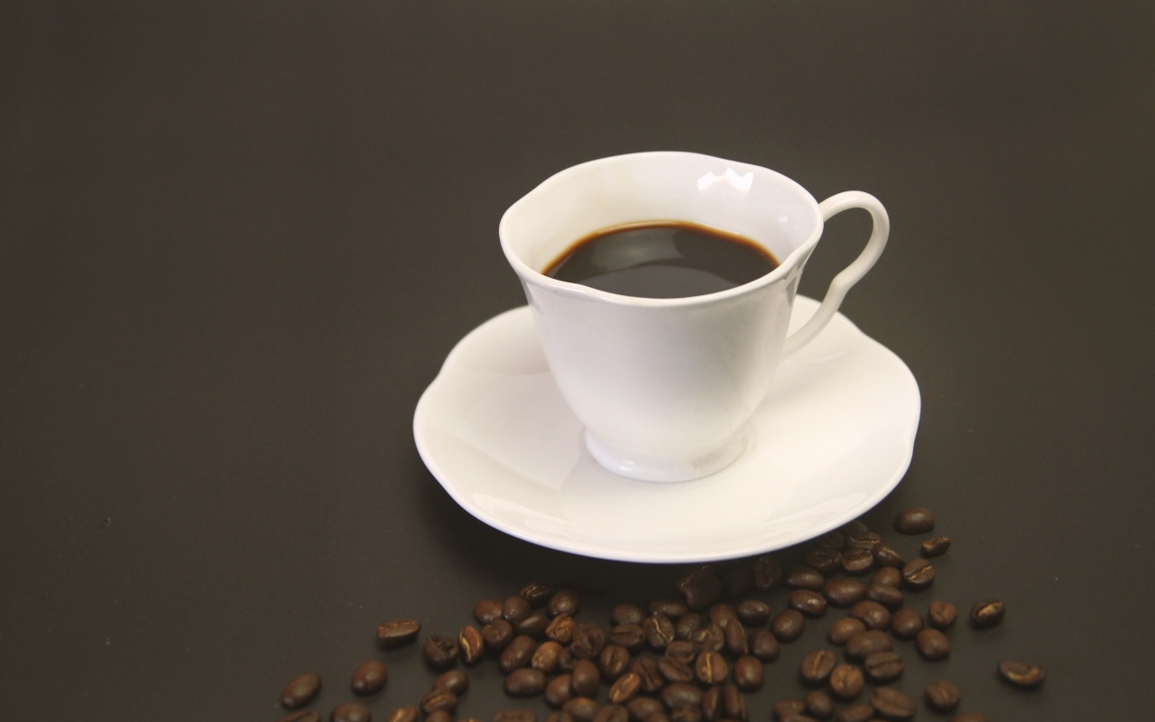 Белая чашка с кофе на столе с зернами