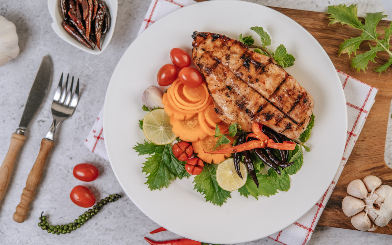 Кусок жареной курицы на большой белой тарелке с овощами