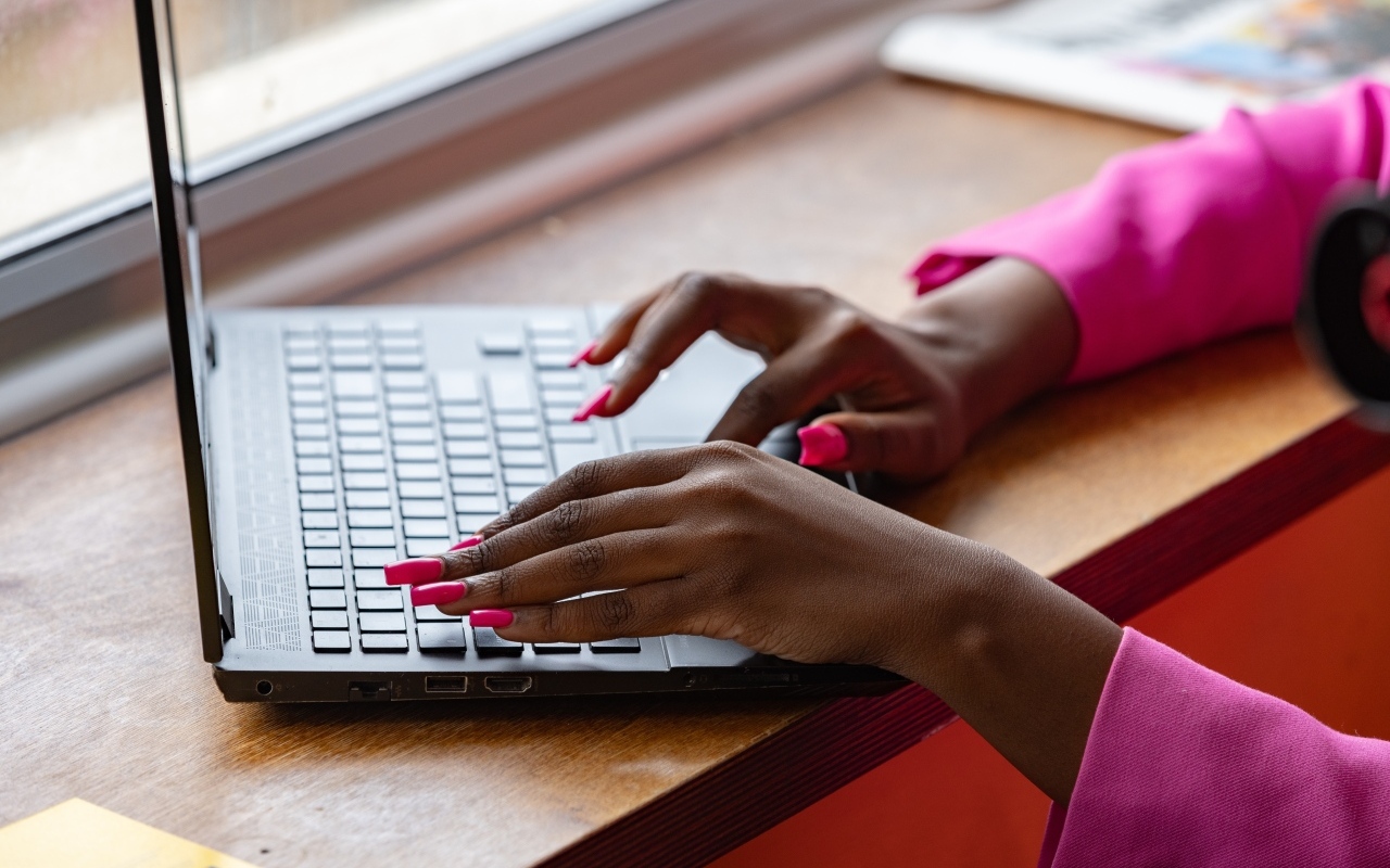 Девушка с розовым маникюром сидит за ноутбуком