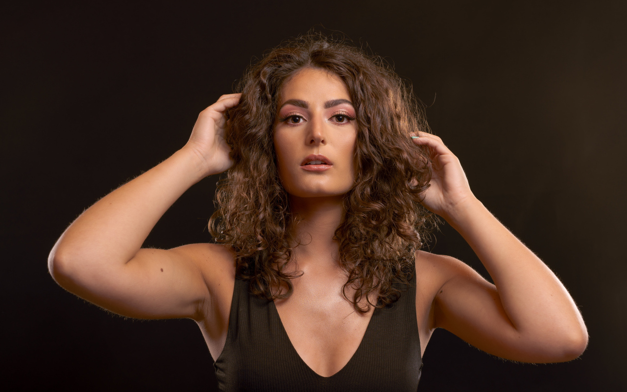 Кудрявая девушка держит руки в волосах на черном фоне