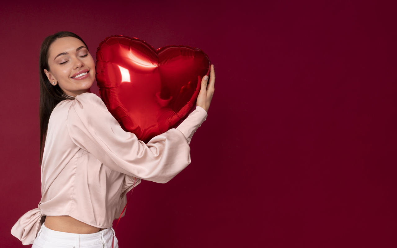 Девушка держит шарик в форме сердца на красном фоне