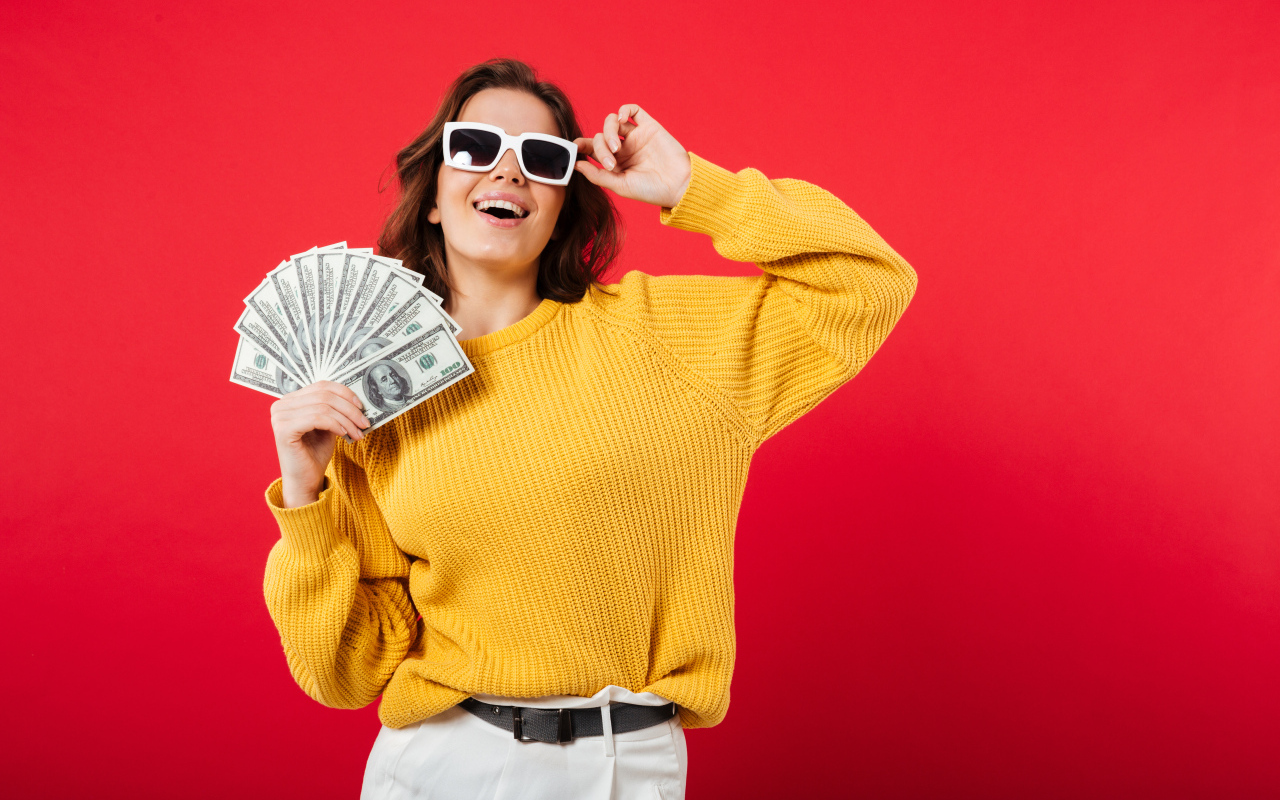 Девушка с веером из долларов на красном фоне