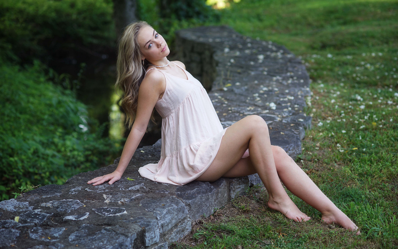 Длинноногая девушка сидит на камне в парке
