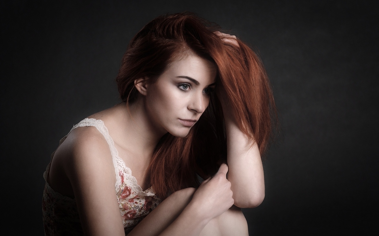 Задумчивая рыжеволосая девушка на сером фоне