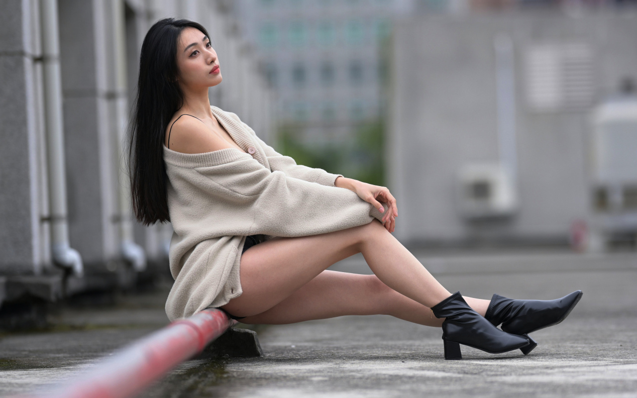 Грустная азиатка в теплой кофте сидит на трубе