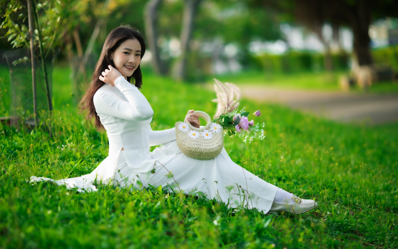 Нежная азиатка в белом наряде сидит на траве