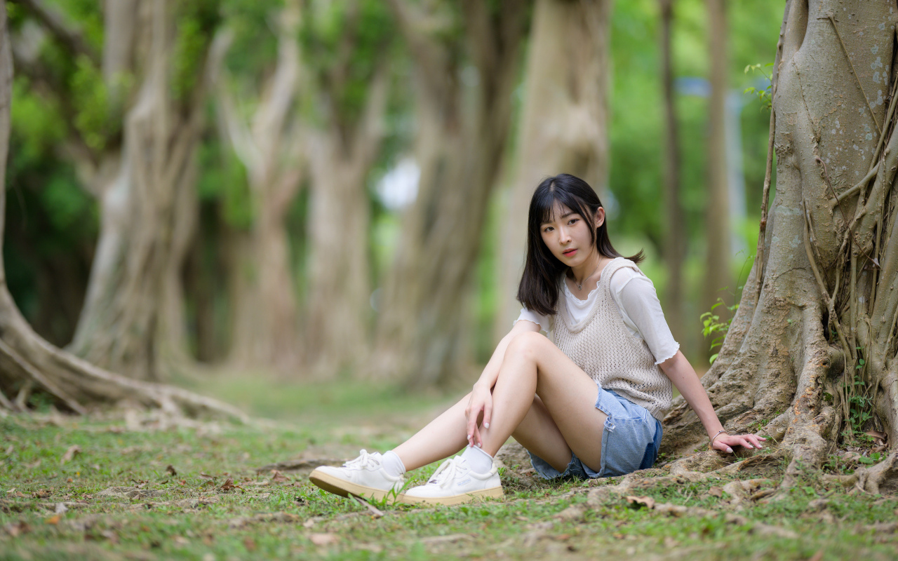 Молодая девушка азиатка сидит у дерева в парке
