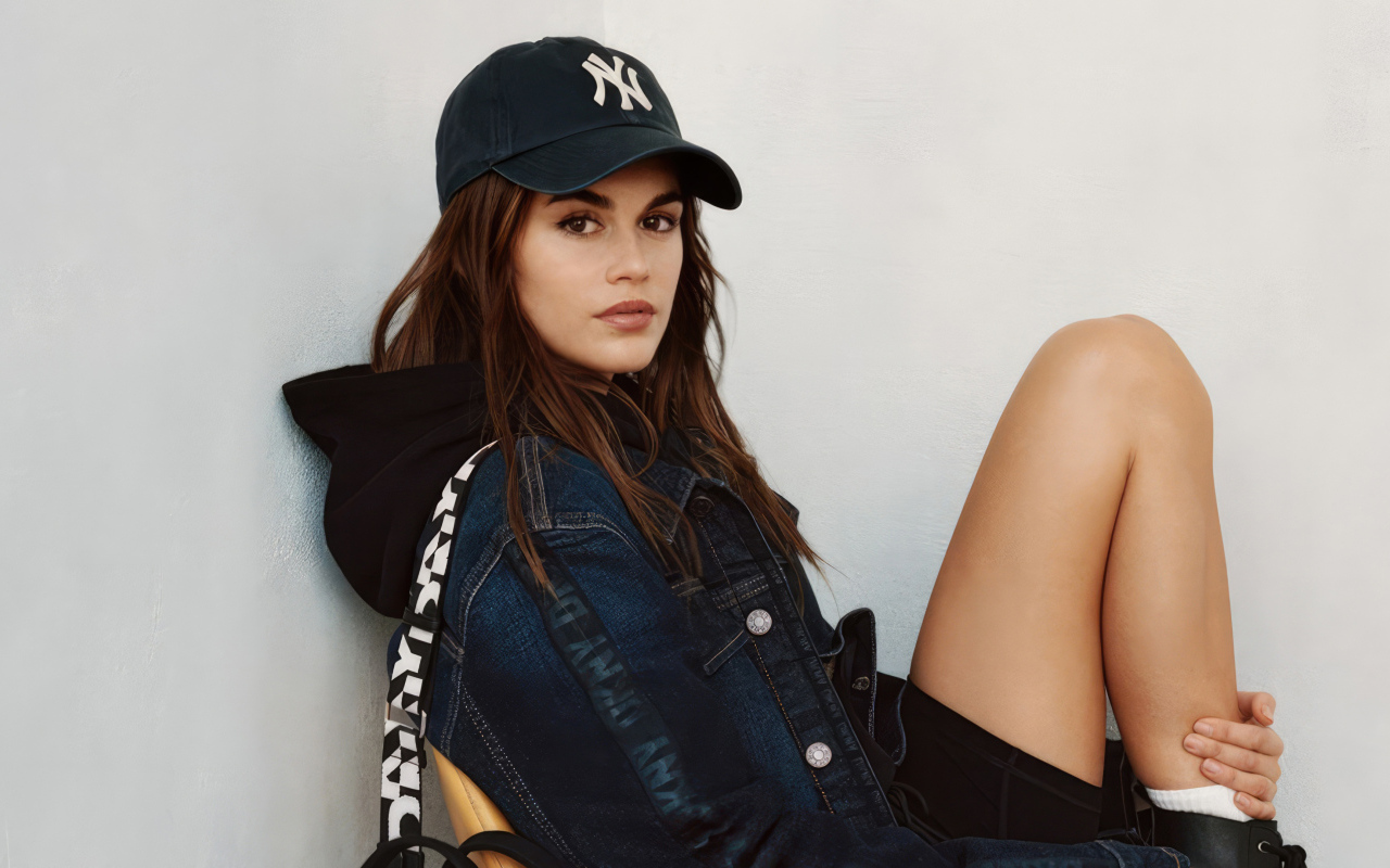 Красивая модель Кайя Гербер в кепке сидит у стены