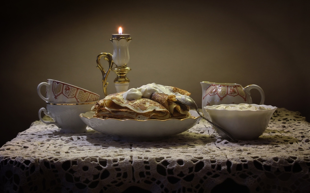 Блины со сметаной на столе со свечой 