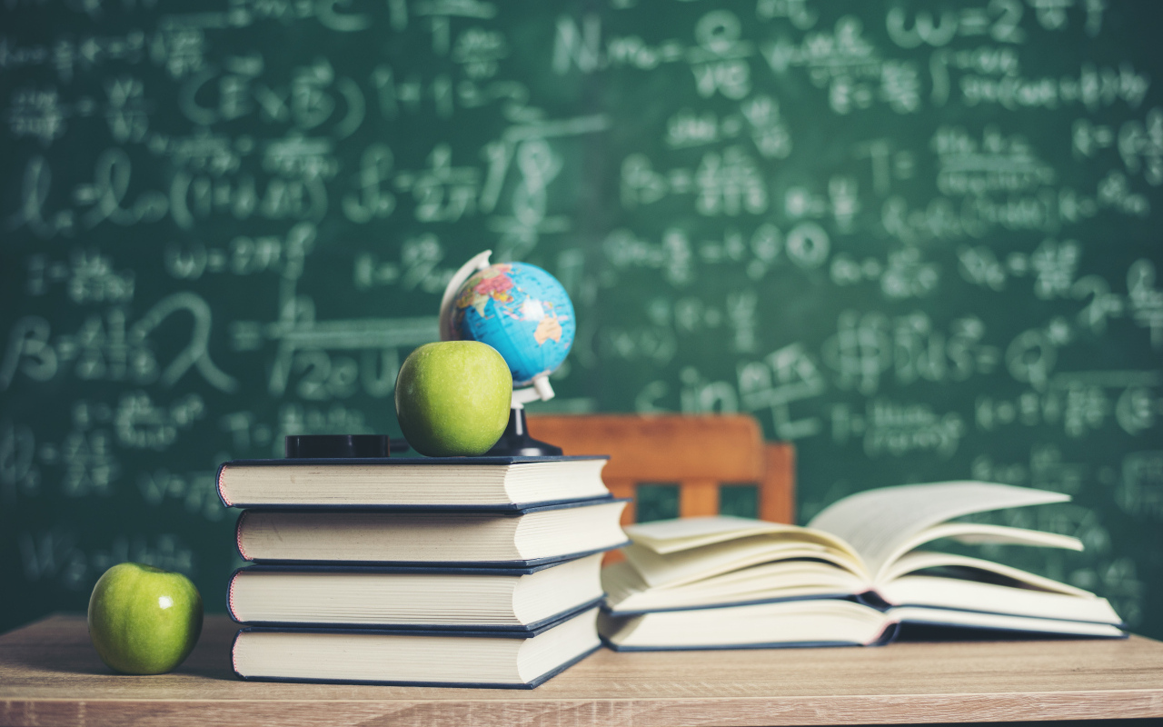 Книги на столе с зелеными яблоками и глобусом на фоне доски