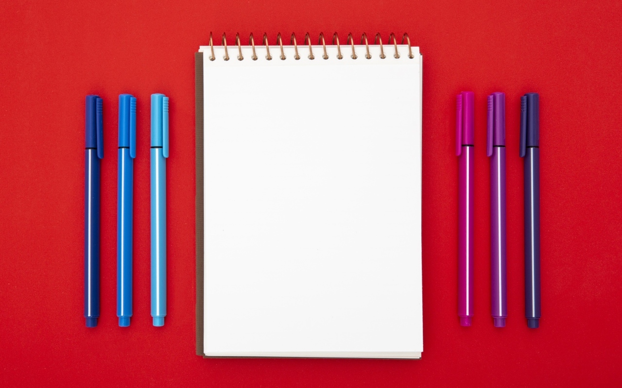 Блокнот и фломастеры на красном фоне