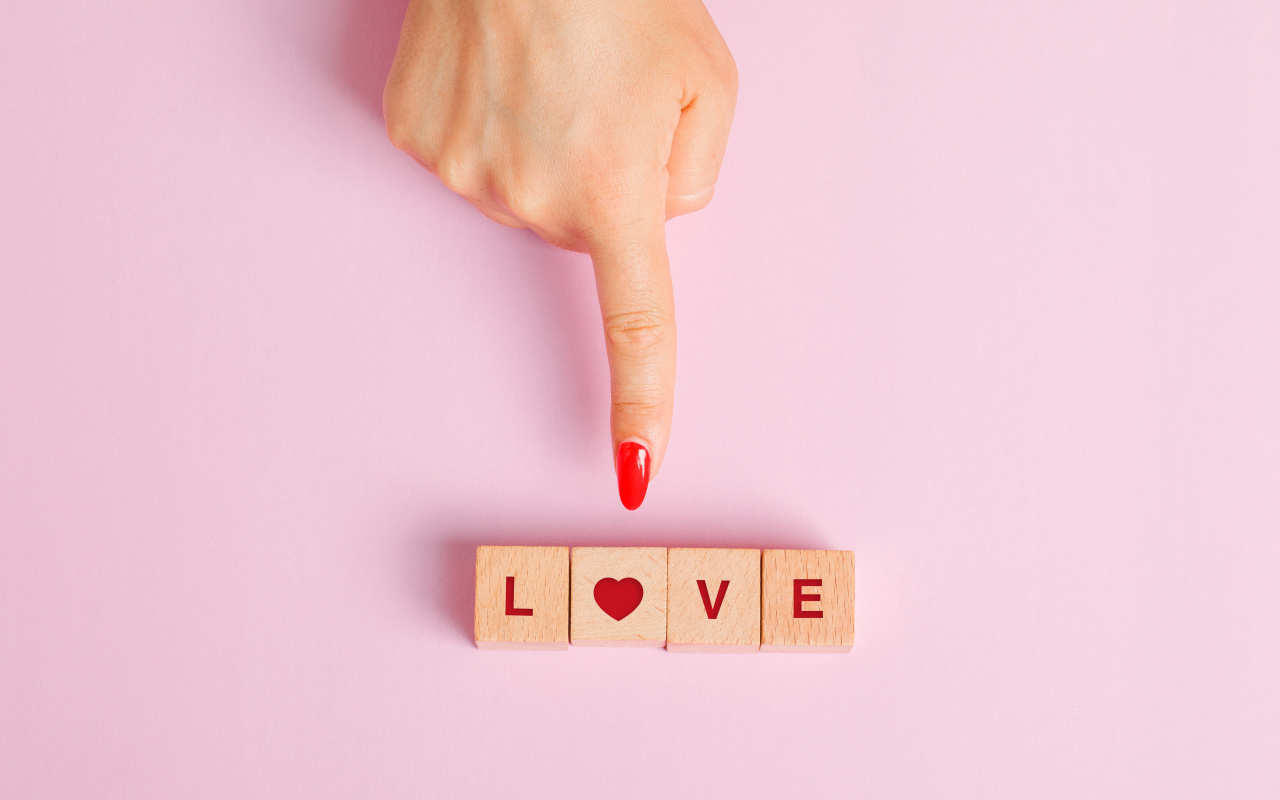Рука указывает на кубики с надписью любовь на розовом фоне