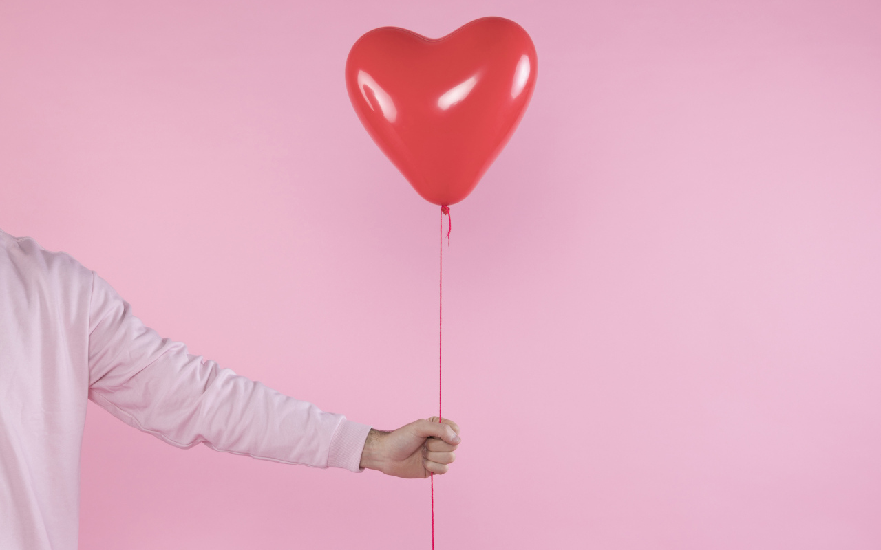 Шарик в форме сердца в руке на розовом фоне