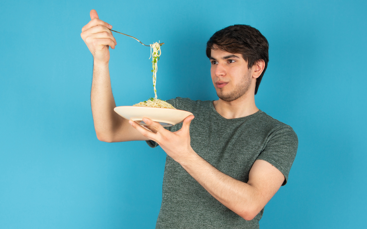 Молодой человек держит тарелку со спагетти в руках