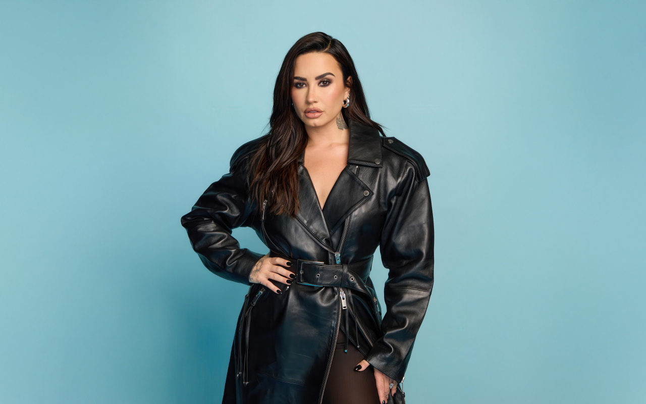 Певица Деми Ловато в кожаном черном пальто на голубом фоне