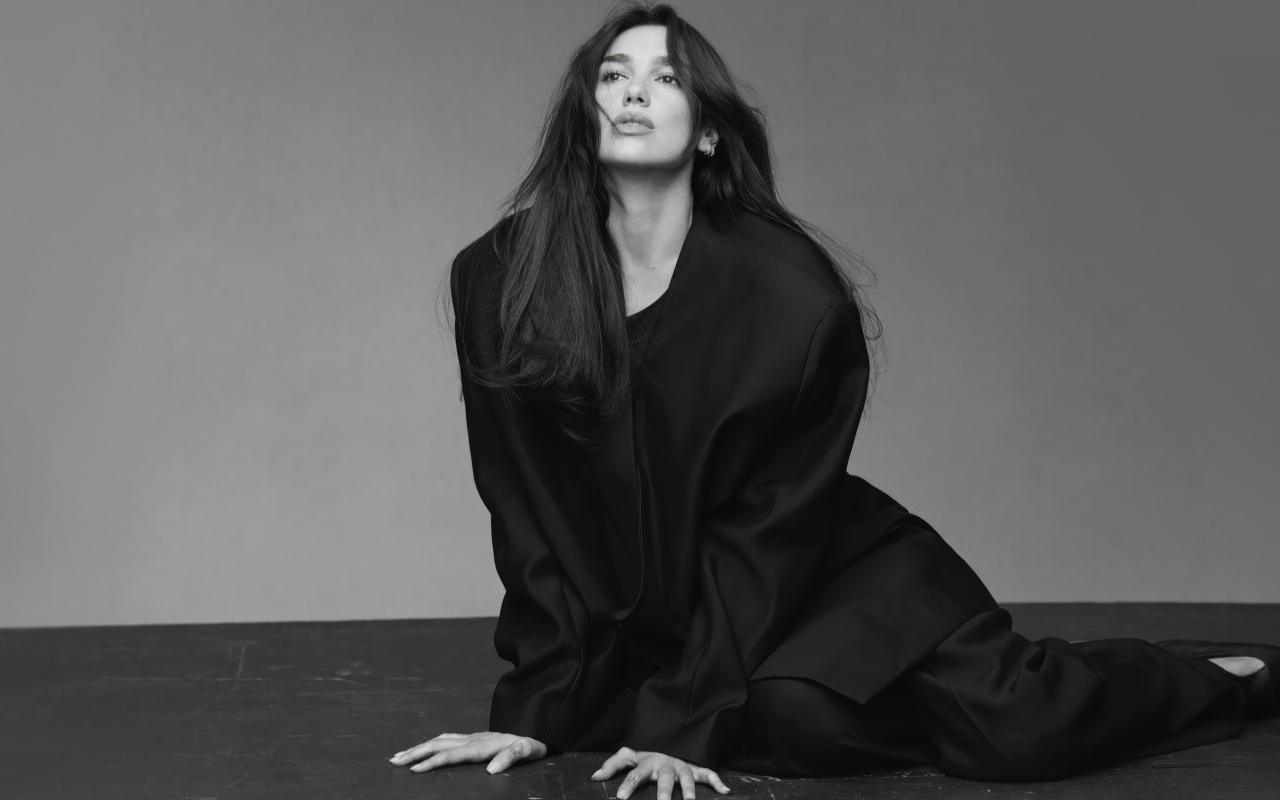 Певица Дуа Липа в черном костюме сидит на полу