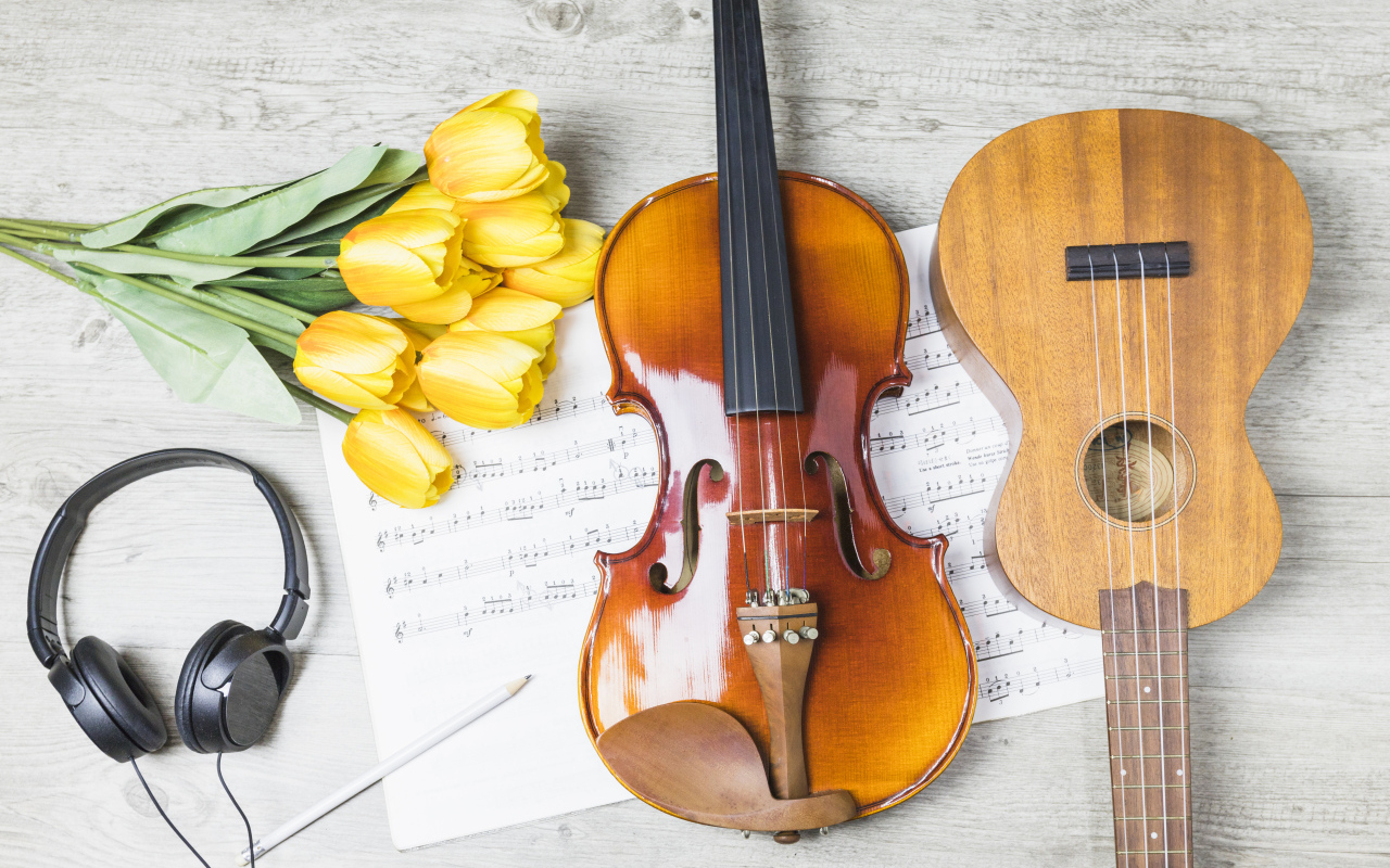 Маленькая гитара и скрипка на столе с нотами, наушниками и букетом тюльпанов