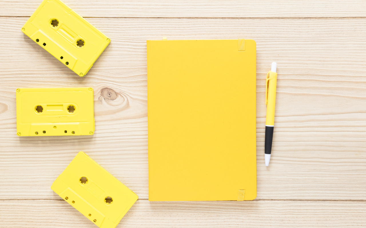 Желтый блокнот с ручкой и кассетами на столе