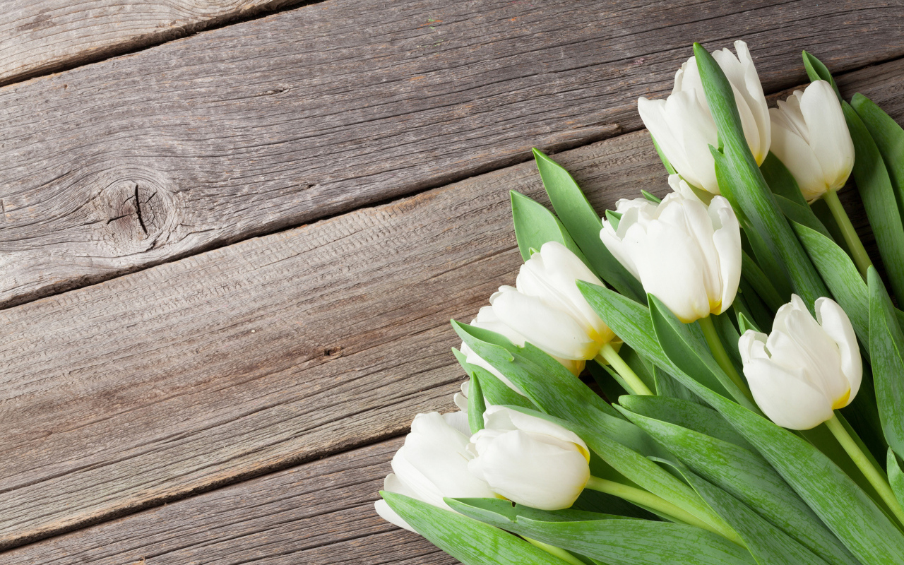 Букет нежных белых тюльпанов с зелеными листьями на деревянном столе