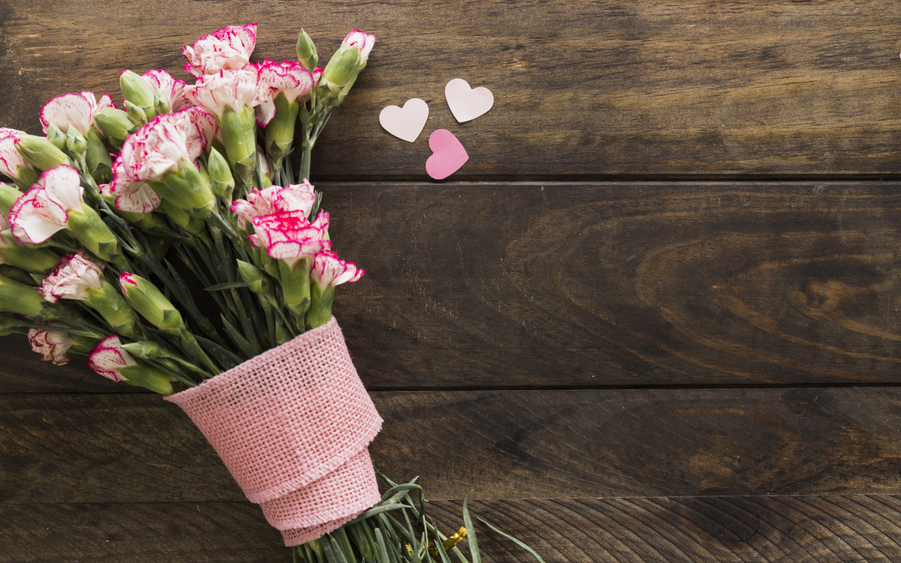 Розовые гвоздики с сердечками на коричневом деревянном фоне