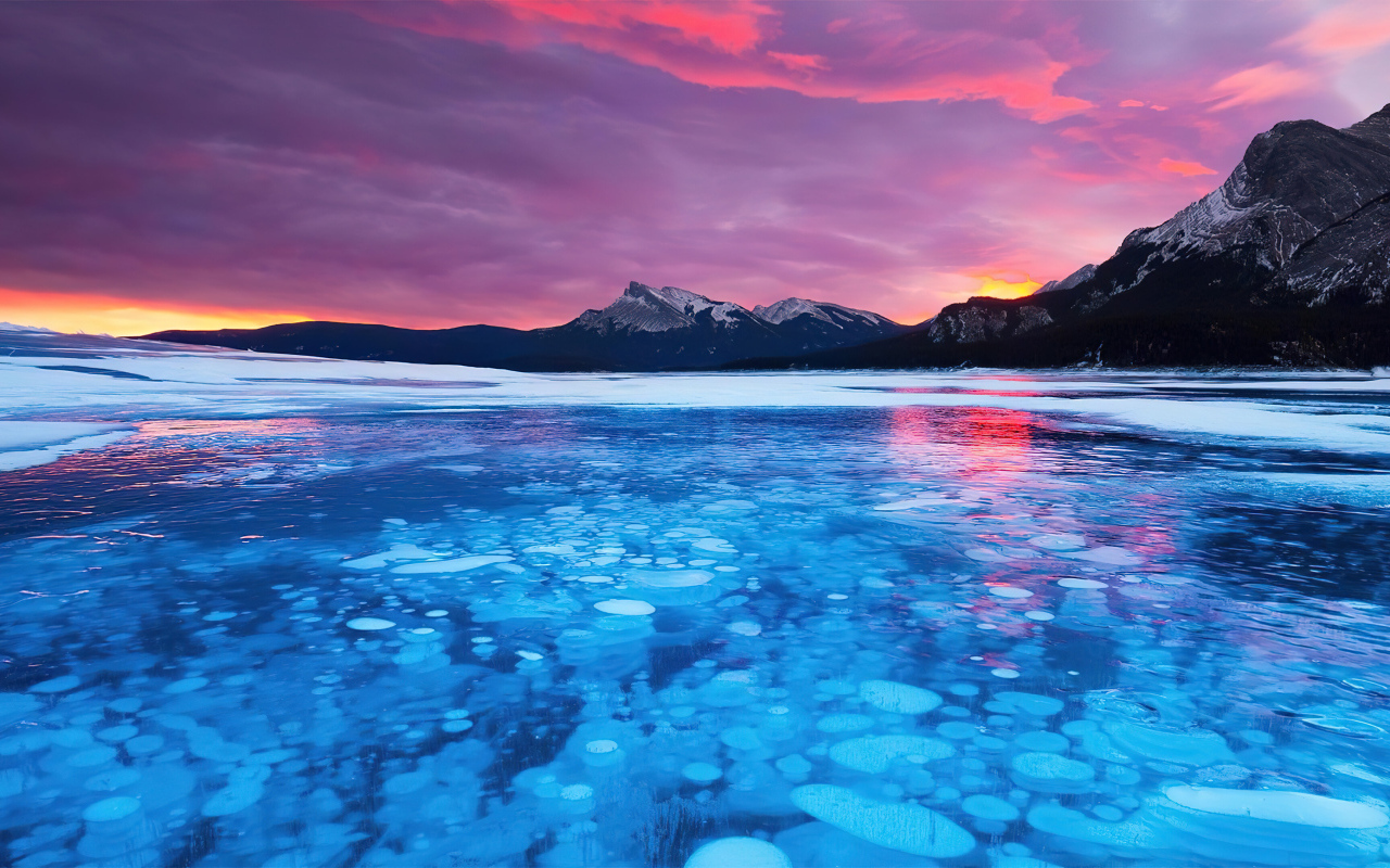 Красный закат солнца над горами у покрытого льдом озера