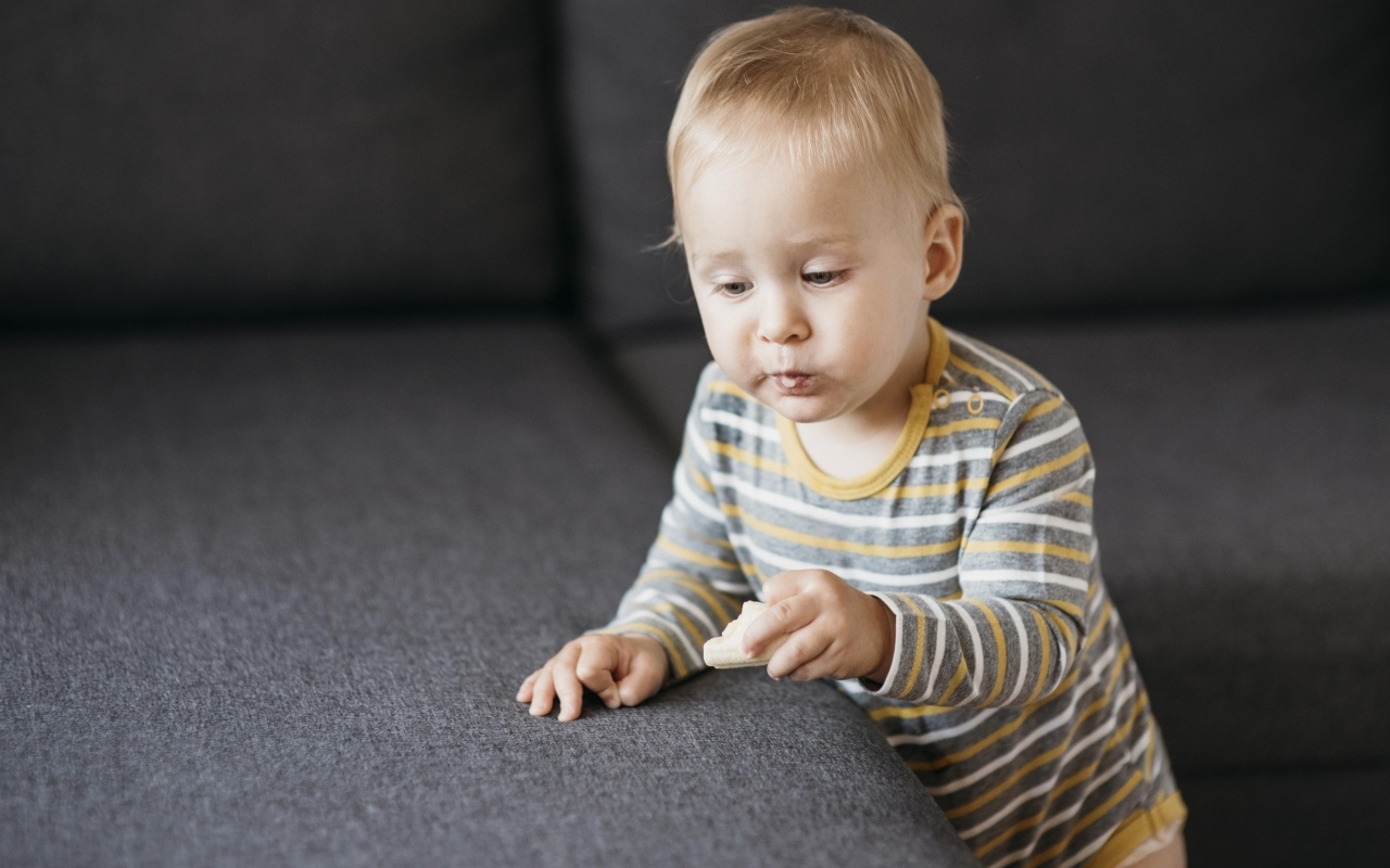 Любопытный маленький ребенок у дивана