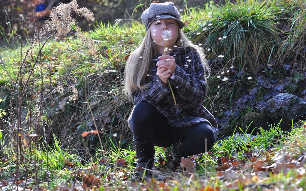 Девочка в кепке дует на одуванчик