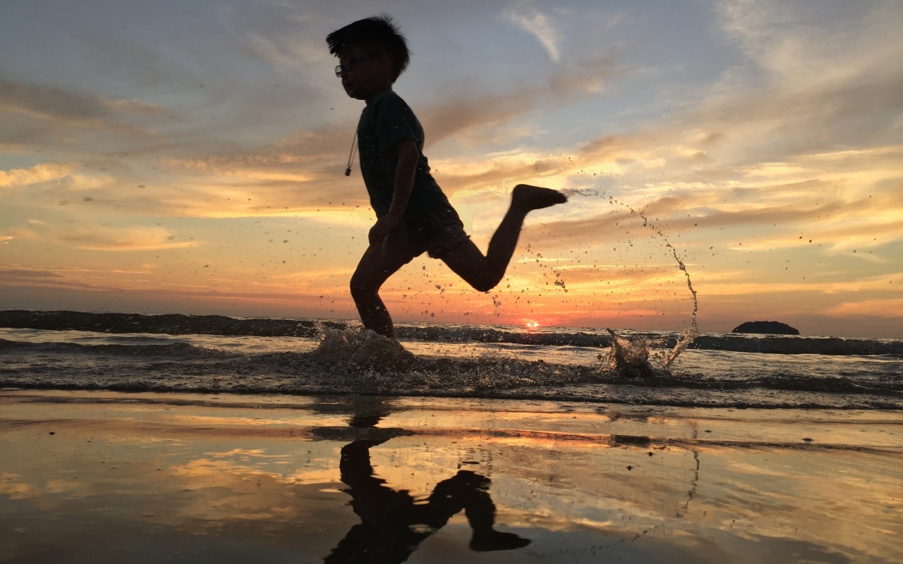 Маленький мальчик бежит по воде на закате