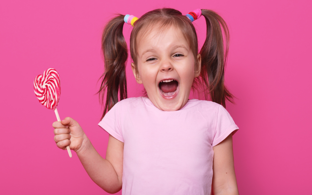 Маленькая девочка с леденцом на розовом фоне