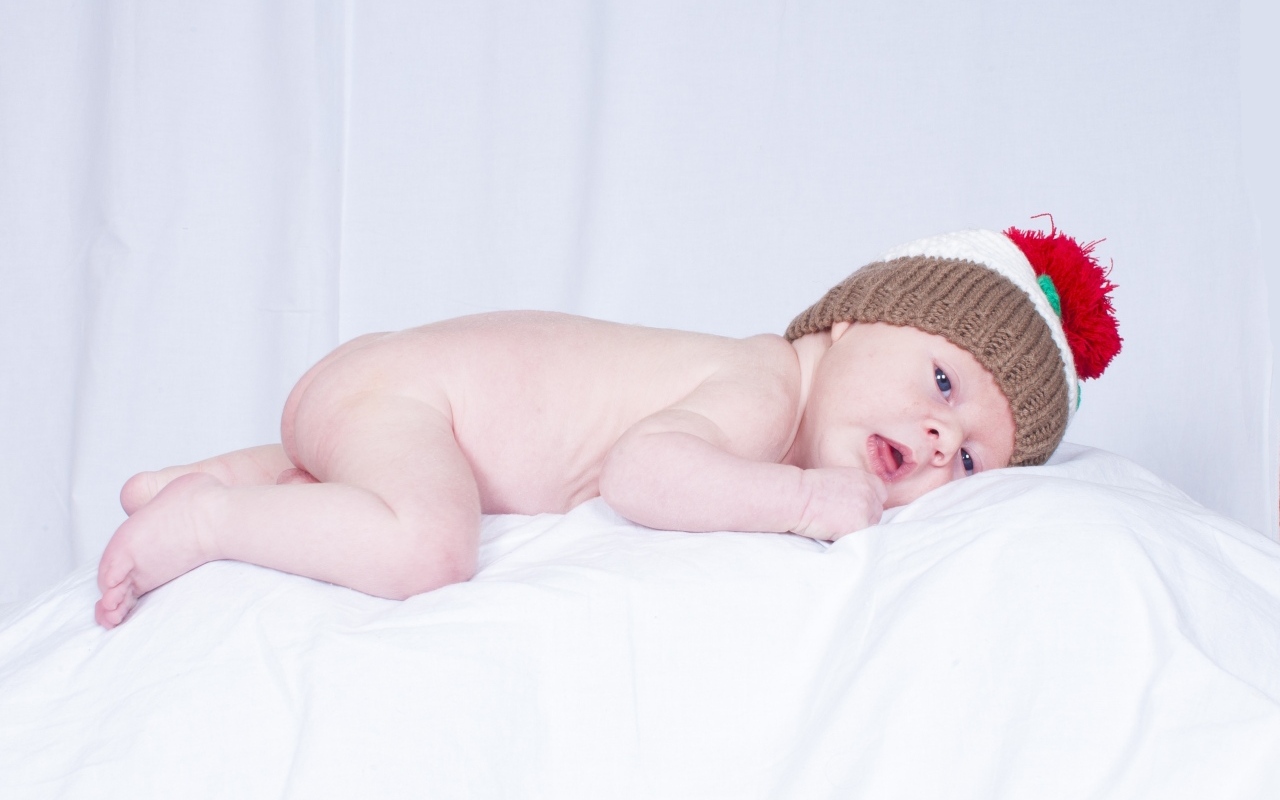 Новорожденный малыш в шапке на белой подушке