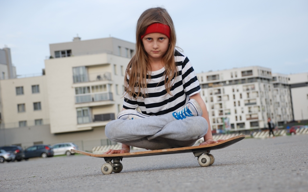Серьезная девочка сидит на  скейтборде