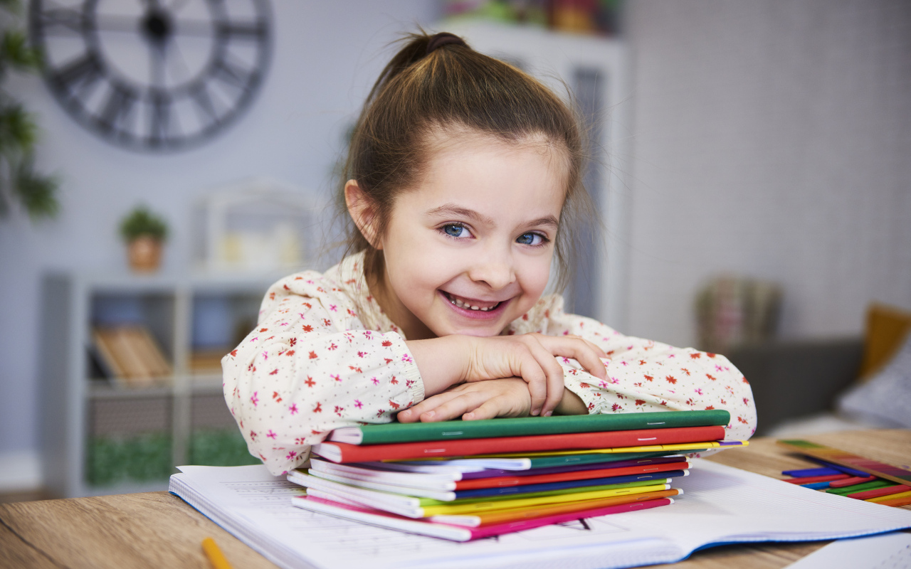 Улыбающаяся девочка ученица  с тетрадями за столом
