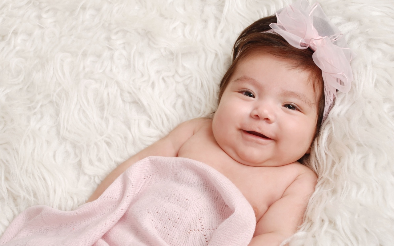 Улыбающаяся новорожденная малышка с бантом на голове