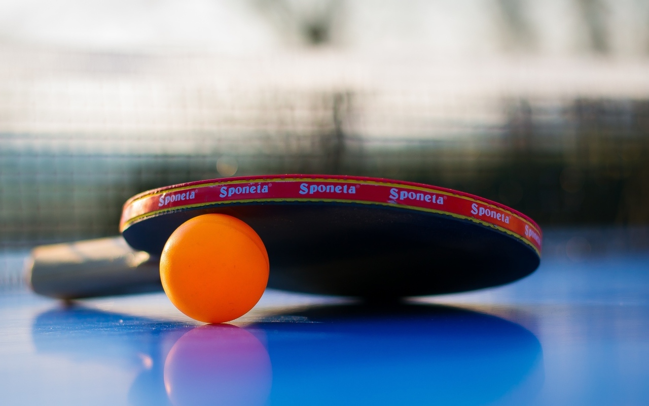 Ракетка и оранжевый мяч для пинг понга на столе